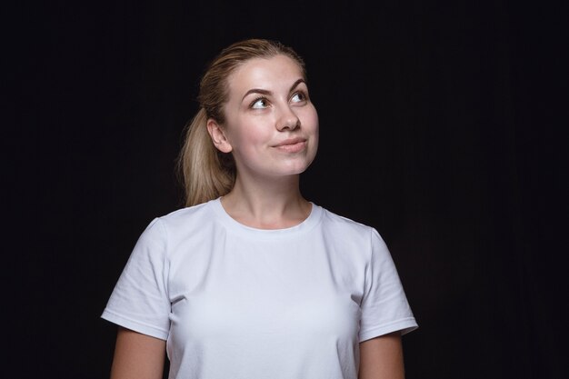 Retrato de mujer joven aislada sobre fondo negro de estudio de cerca. Photoshot de emociones reales de modelo femenino. Soñando y sonriendo, esperanzado y feliz. Expresión facial, concepto de emociones humanas.