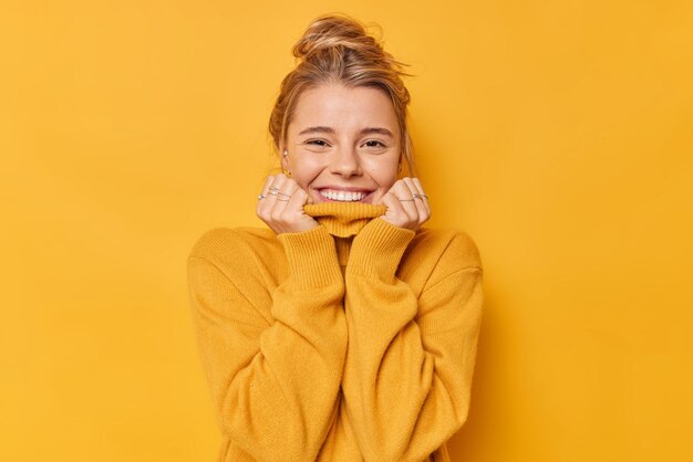 Retrato de mujer joven alegre mantiene las manos en el cuello del puente sonríe con alegría se siente muy feliz ha peinado el cabello aislado sobre fondo amarillo vivo. Concepto de personas y emociones auténticas.