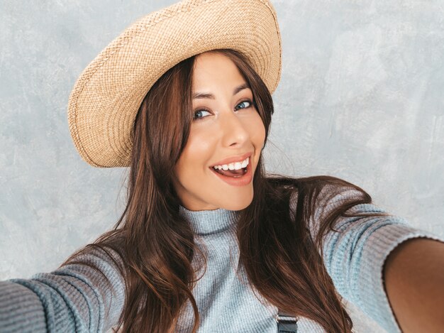 Retrato de mujer joven alegre tomando foto selfie y vistiendo ropa moderna y sombrero.