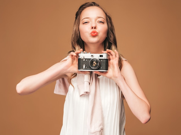 Retrato de mujer joven alegre tomando fotos con inspiración y vestido blanco. Chica sosteniendo la cámara retro. Modelo posando. Dar beso