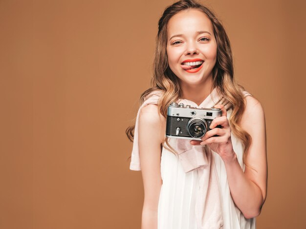 Retrato de mujer joven alegre tomando fotos con inspiración y vestido blanco. Chica sosteniendo la cámara retro. Modelo posando