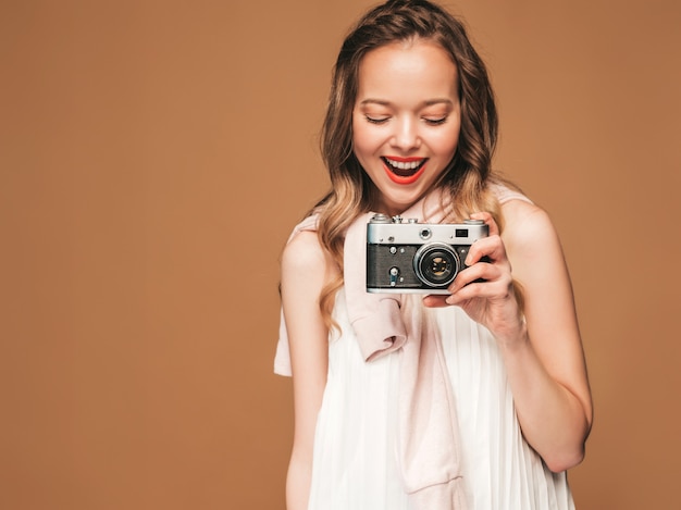 Retrato de mujer joven alegre tomando fotos con inspiración y vestido blanco. Chica sosteniendo la cámara retro. Modelo posando