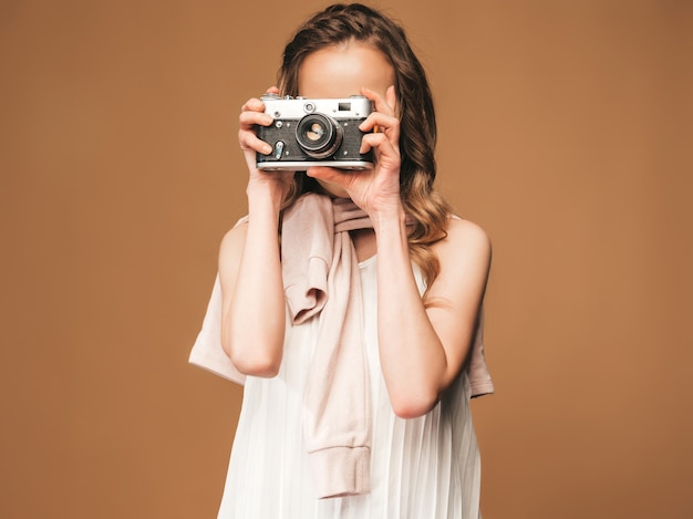 Retrato de mujer joven alegre tomando fotos con inspiración y vestido blanco. Chica sosteniendo la cámara retro. Modelo posando