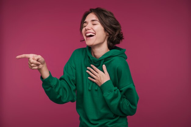 Retrato de una mujer joven apuntando a algo y riendo