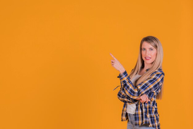 Retrato de una mujer joven apuntando su dedo contra un fondo naranja