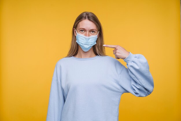 Retrato de una mujer joven apuntando a su máscara médica