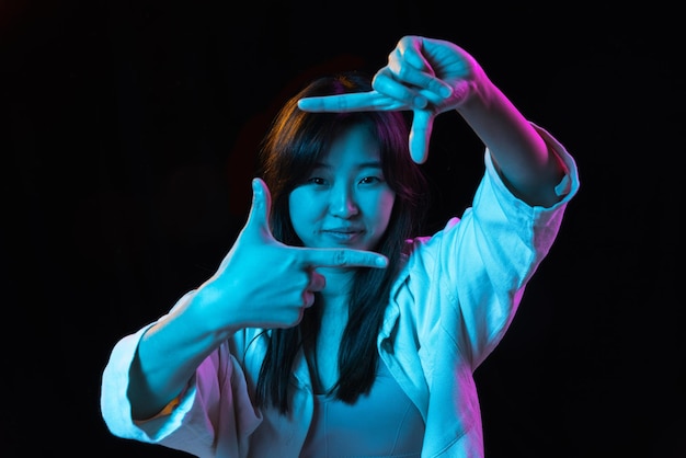Retrato de mujer joven asiática sobre fondo de estudio oscuro en neón Concepto de emociones humanas expresión facial anuncio de ventas para jóvenes