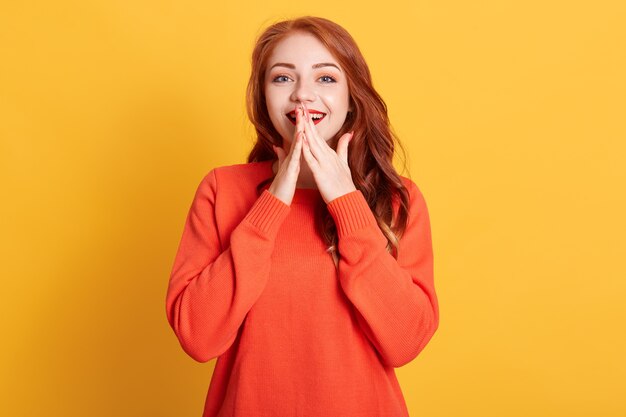 Retrato de mujer joven asombrada posando con expresión facial emocionada aislada, manteniendo las manos en la boca