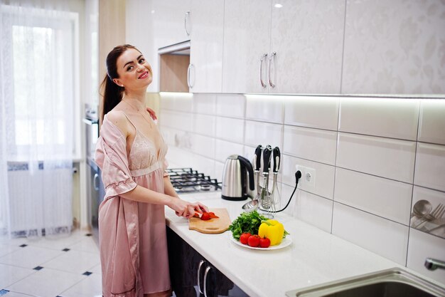 Retrato de una mujer joven atractiva en bata haciendo ensalada de verduras frescas en la cocina