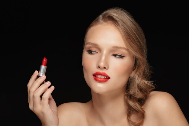 Retrato de mujer joven y atractiva con cabello ondulado mirando soñadoramente con lápiz labial rojo sobre fondo negro aislado