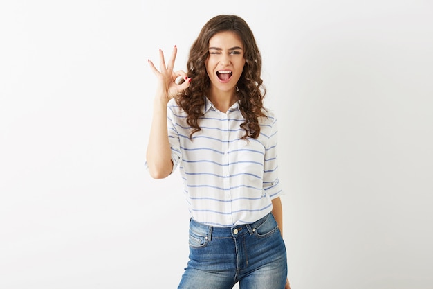 Retrato de mujer joven y atractiva con expresión de la cara emocionada que muestra un gesto positivo, sonriente, feliz, guiñando un ojo, estilo hipster, pelo rizado aislado, signo bien, estado de ánimo alegre, cara hermosa