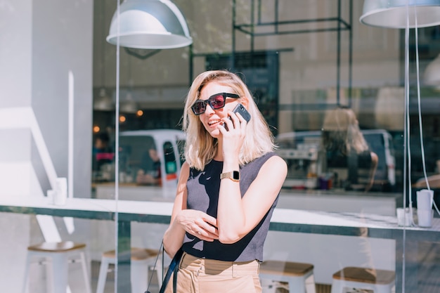 Retrato de una mujer joven atractiva que se coloca delante de la tienda que habla en el teléfono móvil