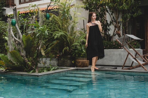 Retrato de mujer joven y atractiva en vestido elegante, sombrero de paja, estilo de verano, tendencia de moda, vacaciones, sonriendo, accesorios elegantes, gafas de sol, posando en villa tropical en Bali
