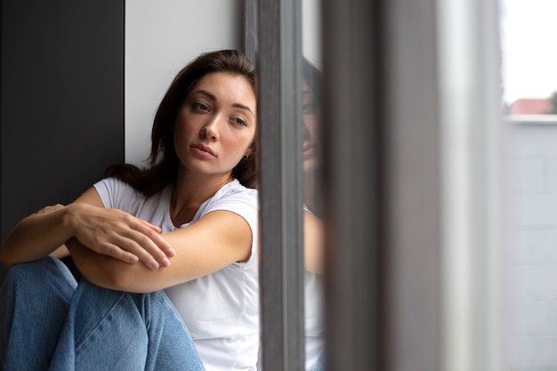 Retrato de mujer joven con baja autoestima sentada junto a la ventana en casa