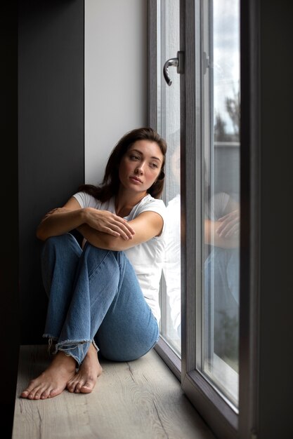 Retrato de mujer joven con baja autoestima sentada junto a la ventana en casa