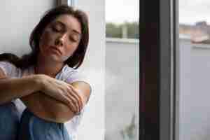 Foto gratuita retrato de mujer joven con baja autoestima sentada junto a la ventana en casa