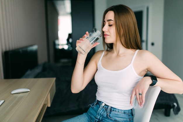 Retrato de una mujer joven bebiendo agua en la cocina de casa