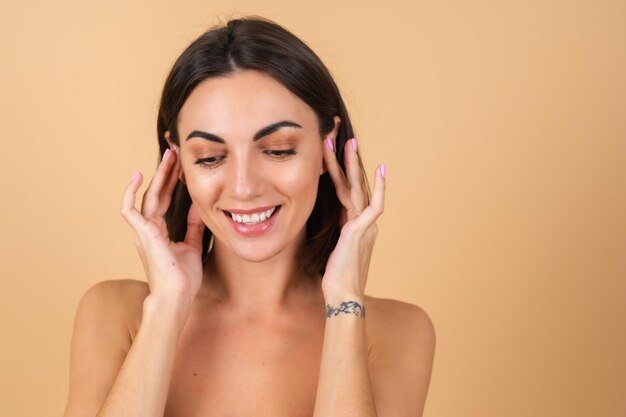 Retrato de una mujer joven en beige con maquillaje natural, con una ligera sonrisa sensual, hombros desnudos, rostro de belleza, publicidad de cosméticos y cuidado.