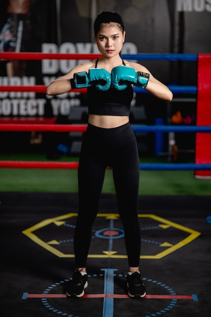 Retrato de mujer joven y bonita en guantes de boxeo pose de pie sobre lienzo en el gimnasio, clase de boxeo de entrenamiento de niña sana,