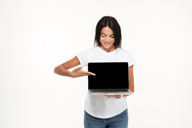 Retrato de una mujer joven y bonita que presenta portátil con pantalla en blanco