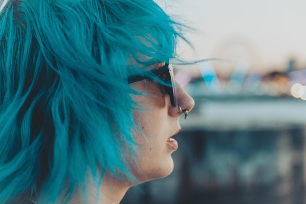 Retrato de una mujer joven con cabello azul y rosa con gafas de sol con un fondo borroso