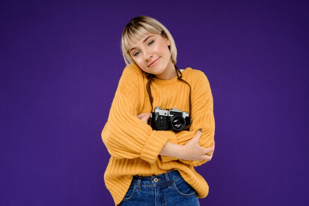 Retrato de mujer joven con cámara sobre pared púrpura