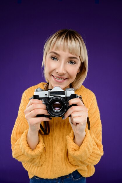 Retrato de mujer joven con cámara sobre pared púrpura