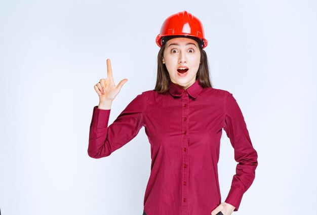 Retrato de mujer joven en casco apuntando hacia arriba.