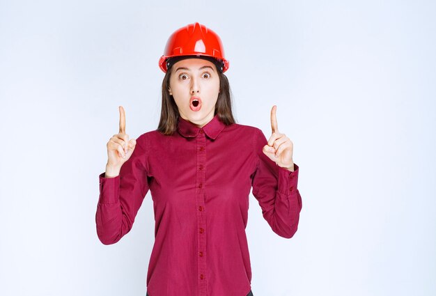 Retrato de mujer joven en casco apuntando hacia arriba.