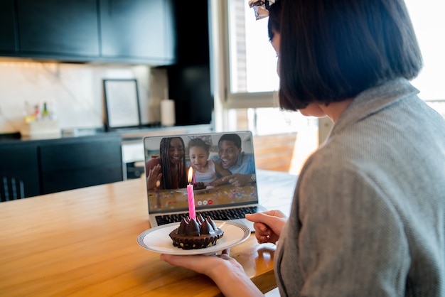 Retrato de mujer joven celebrando un cumpleaños en una videollamada con un portátil y un pastel desde casa