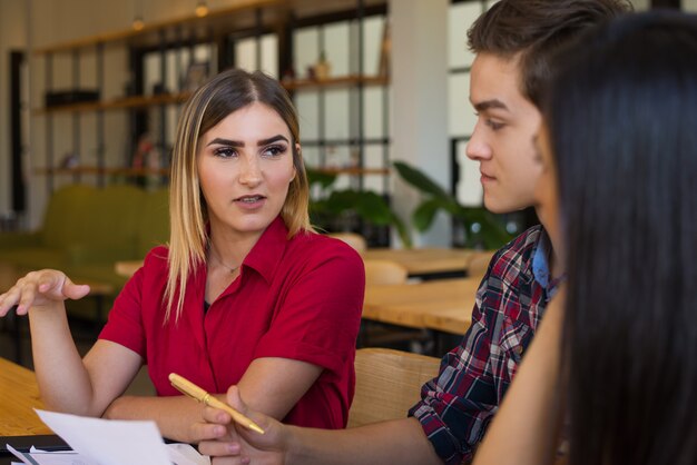 Retrato de la mujer joven confiada que habla con sus amigos en café