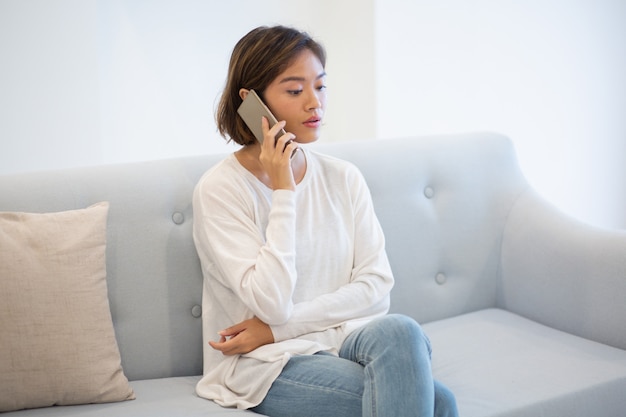 Retrato de la mujer joven confiada que habla en el teléfono móvil en casa