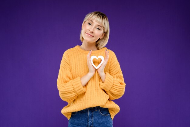 Retrato de mujer joven con corazón de decoración sobre pared púrpura