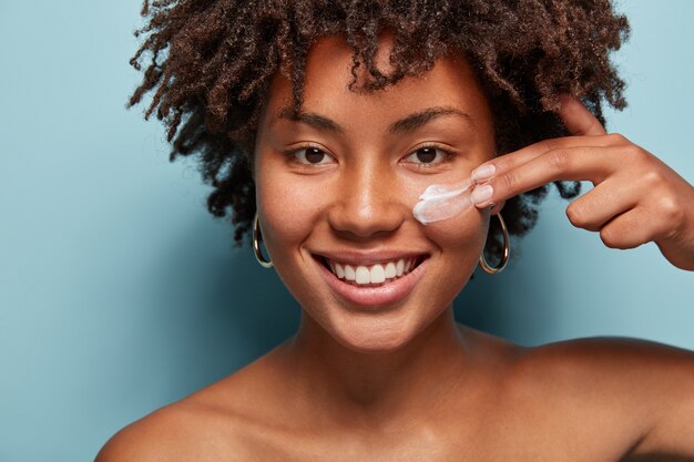 Retrato de mujer joven con corte de pelo afro aplicando crema