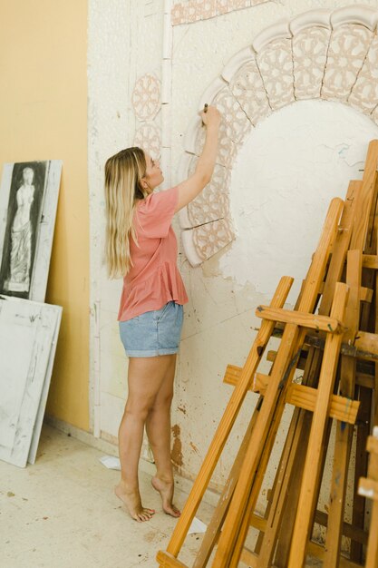 Retrato de mujer joven creativa talla en la pared con herramienta