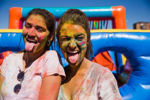 Retrato de una mujer joven cubierta con cara de holi sacando la lengua mirando a la cámara