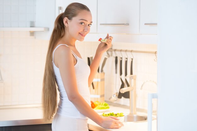 Retrato de una mujer joven degustación de una ensalada verde en la cocina,
