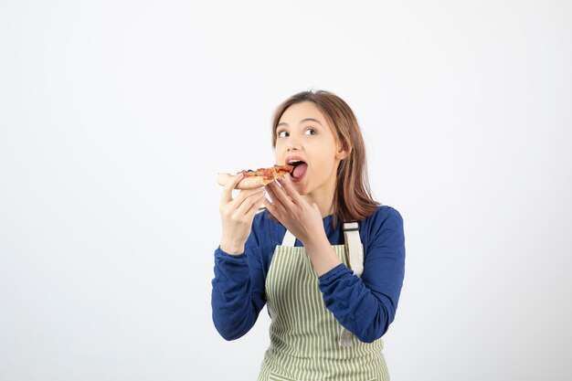 Retrato de mujer joven en delantal comiendo pizza en blanco