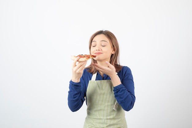 Retrato de mujer joven en delantal comiendo pizza en blanco