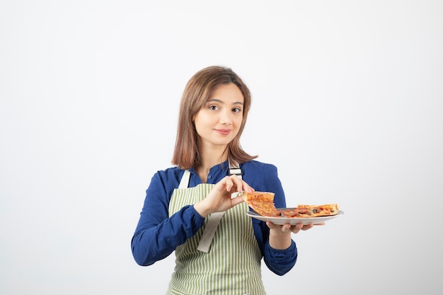 Retrato de mujer joven en delantal mostrando porciones de pizza en blanco