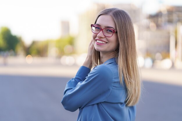 Retrato de mujer joven despreocupada sonriendo con calle urbana. Alegre niña caucásica con anteojos en la ciudad.