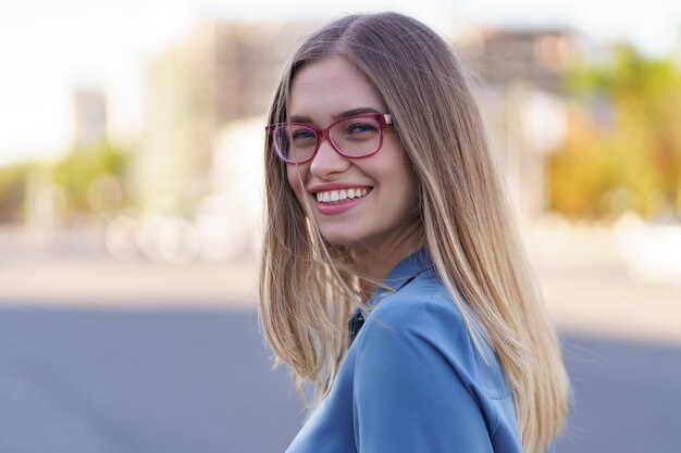 Retrato de mujer joven despreocupada sonriendo con calle urbana. Alegre niña caucásica con anteojos en la ciudad.