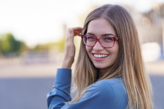 Retrato de mujer joven despreocupada sonriendo con calle urbana. Alegre niña caucásica con anteojos en la ciudad.