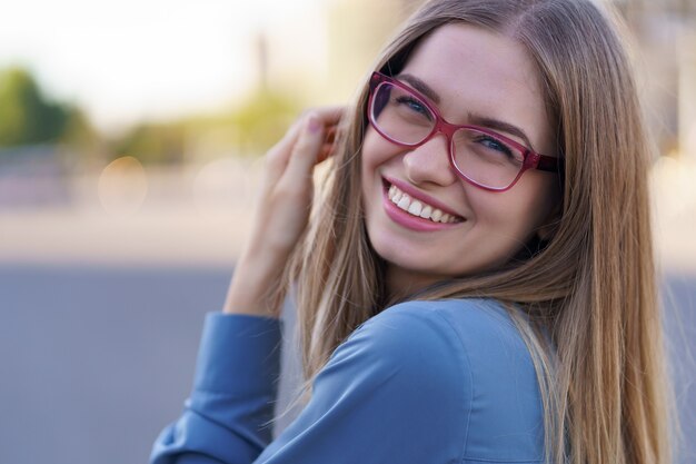 Retrato de mujer joven despreocupada sonriendo con calle urbana. Alegre niña caucásica con anteojos en la ciudad.