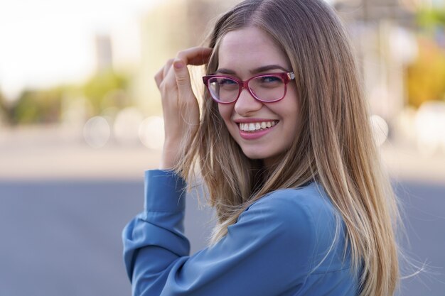 Retrato de mujer joven despreocupada sonriendo con calle urbana. Alegre niña caucásica con anteojos en la ciudad.