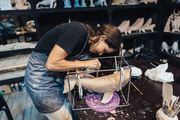 Retrato de mujer joven disfrutando de su trabajo favorito en el taller. El alfarero trabaja con cuidado en la ballena de arcilla