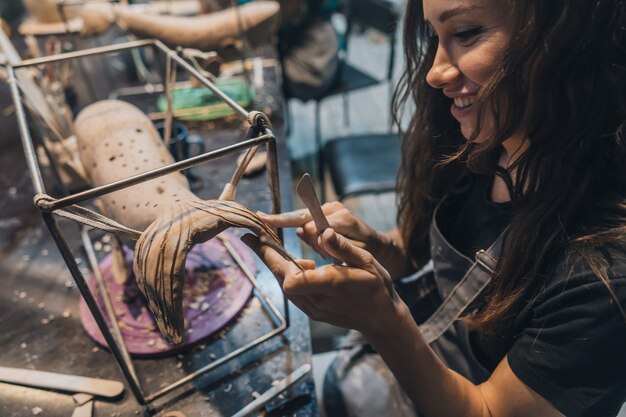 Retrato de mujer joven disfrutando de su trabajo favorito en el taller. El alfarero trabaja con cuidado en la ballena de arcilla