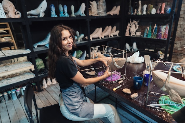 Retrato de mujer joven disfrutando de su trabajo favorito en el taller. alfarero trabaja cuidadosamente en la ballena de arcilla