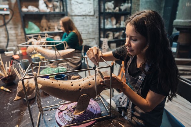 Retrato de mujer joven disfrutando de su trabajo favorito en el taller. alfarero trabaja cuidadosamente en la ballena de arcilla