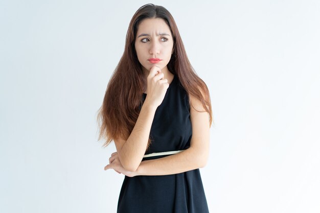 Retrato de mujer joven dudosa de pie con la mano en la barbilla